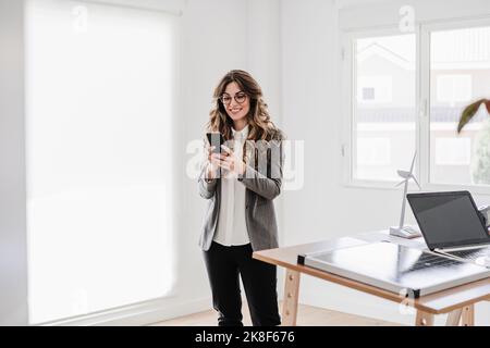Young businesswoman standing in office reading text meassge Stock Photo