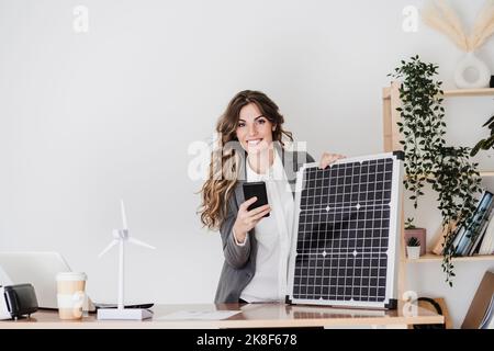 Modern businesswoman with smartphone using portable solar module in office Stock Photo