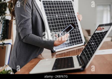 Modern businesswoman with smartphone using portable solar module in office Stock Photo