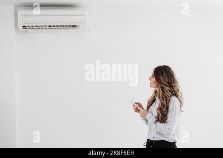 Businesswoman switching on air conditioning in the office Stock Photo