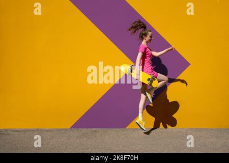 Woman with skateboard jumping in front of patterned wall Stock Photo