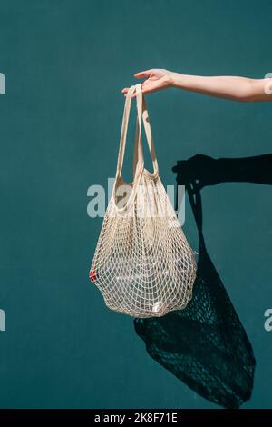 Hand of woman holding mesh bag with plastic bottles in front of wall Stock Photo