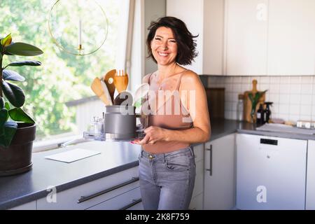 Happy woman holding cooking utensils in container on tray at home Stock Photo