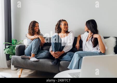 Multiracial friends talking and sitting on couch at home Stock Photo