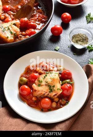 Cod stew with chickpeas, cherry tomatoes and olives on plate over dark stone background. Stock Photo