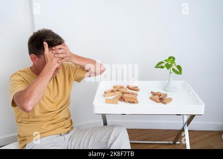 Frustrated mature man with fallen wooden blocks on coffee table at home Stock Photo