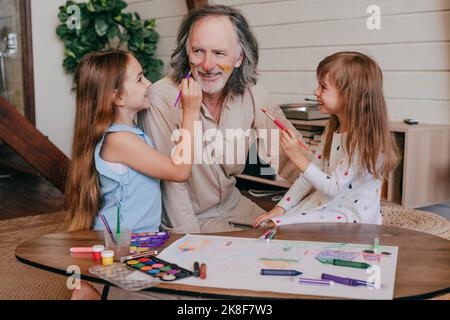 Granddaughters having fun painting grandfather's face at home Stock Photo