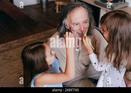 Playful children having fun painting grandfather's nose at home Stock Photo