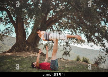 Young couple practicing acroyoga under oak tree Stock Photo