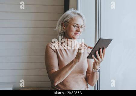 Smiling woman using tablet PC standing by window at home Stock Photo