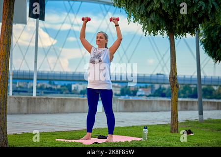 Mature woman exercising with weights in park Stock Photo