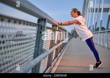 Woman exercising near railing on bridge Stock Photo