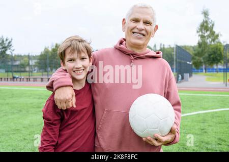 Smiling retired senior man holding soccer ball with arm around grandson Stock Photo