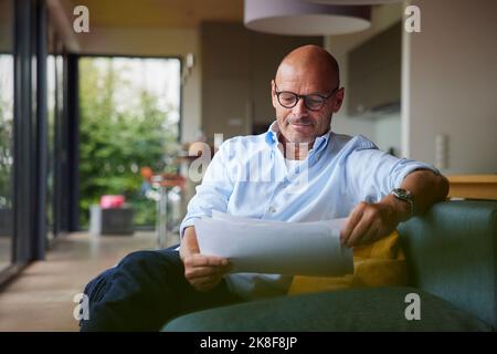 Senior man reading documents sitting on sofa at home Stock Photo