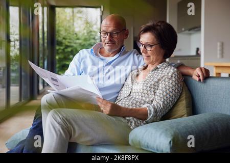 Smiling man with woman reading documents at home Stock Photo