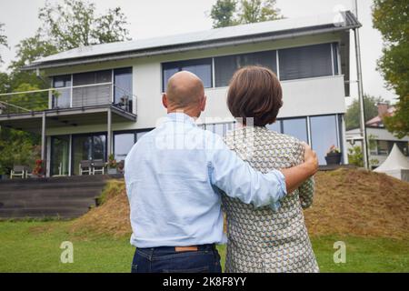 Senior couple standing together in front of house Stock Photo