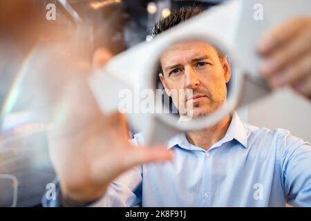 Concentrated mature engineer examining machine part at factory Stock Photo