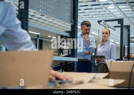 Businessman standing by businesswoman looking at engineer working in factory Stock Photo