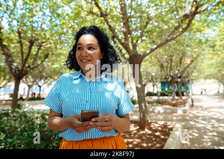 Contemplative woman with smart phone in front of trees at park Stock Photo