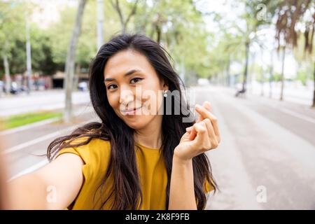 Smiling woman making taking selfie on tree-lined street in the city Stock Photo