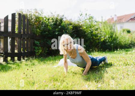 Senior woman practicing push-ups on grass in garden Stock Photo