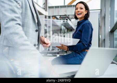 Happy businessman holding note pad looking at businessman with laptop in industry Stock Photo
