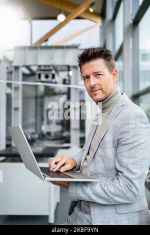 Mature businessman holding laptop standing in industry Stock Photo