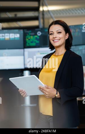 Smiling businesswoman holding tablet PC in front of computer monitors Stock Photo