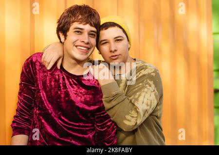 Happy non-binary couple standing in front of yellow corrugated wall Stock Photo