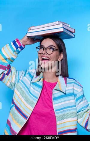 Happy woman wearing colorful zipper holding books on head against blue background Stock Photo