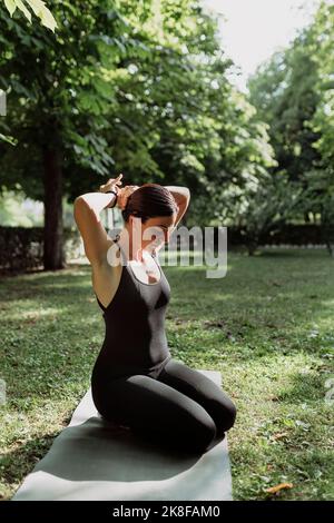 Yoga teacher tying hair sitting on exercise mat in park Stock Photo