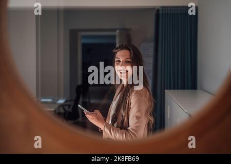Happy young businesswoman with smart phone seen through glass Stock Photo
