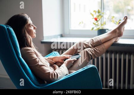 Thoughtful young businesswoman sitting on chair with feet up at home Stock Photo