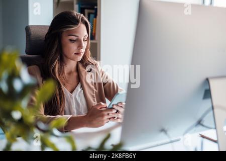 Young freelancer text messaging through smart phone sitting in home office Stock Photo