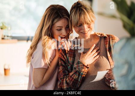 Excited woman with pregnant sister holding ultrasound at home Stock Photo