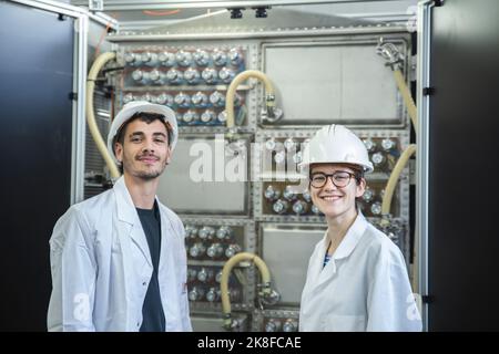 Smiling engineers with hardhat by machine in factory Stock Photo