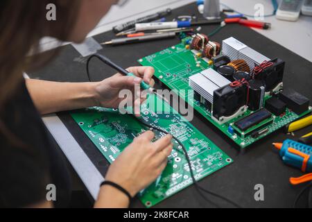 Woman soldering motherboard on table in workshop Stock Photo