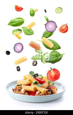 Plate with tasty pasta salad and falling ingredients on white background Stock Photo