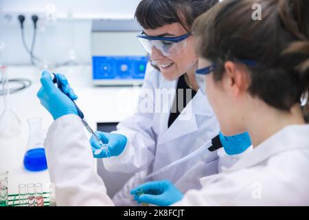 Smiling scientist using pipette for experimenting with coworker in laboratory Stock Photo
