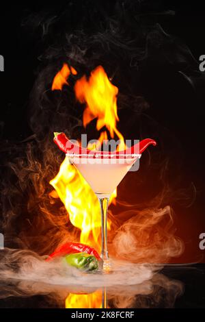 Glass of tasty margarita cocktail with chili pepper and fire flame on dark color background Stock Photo