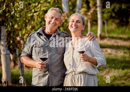 Happy mature couple holding red wineglasses in front of vineyard Stock Photo
