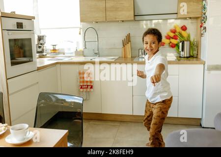 Happy boy gesturing fists standing in kitchen Stock Photo