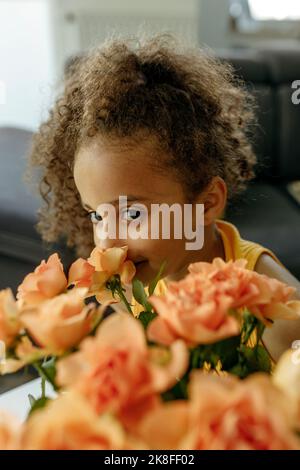 Smiling girl smelling orange roses at home Stock Photo