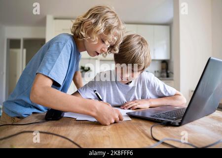 Boy assisting brother doing homework at home Stock Photo