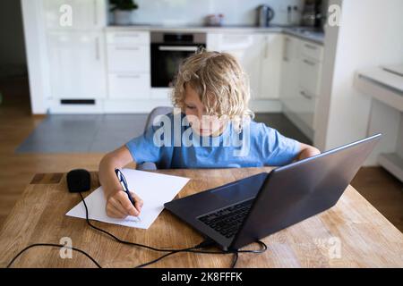 Boy doing homework with laptop on table at home Stock Photo