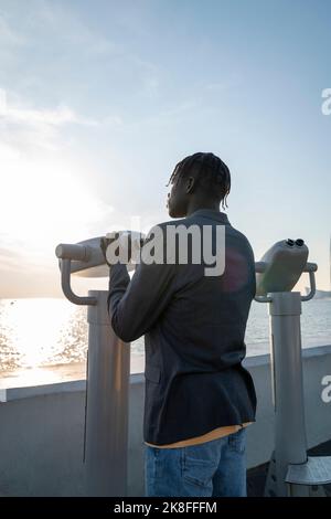 Young businessman in front of coin-operated binoculars on footpath Stock Photo