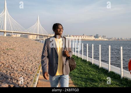 Smiling young businessman with backpack walking on footpath Stock Photo