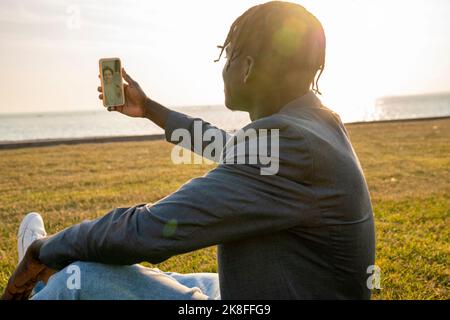 Businessman having video call through smart phone sitting on grass Stock Photo