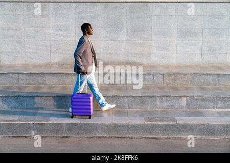 Smiling young businessman with suitcase walking on step Stock Photo