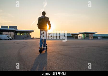 Businessman riding electric push scooter on street at sunset Stock Photo